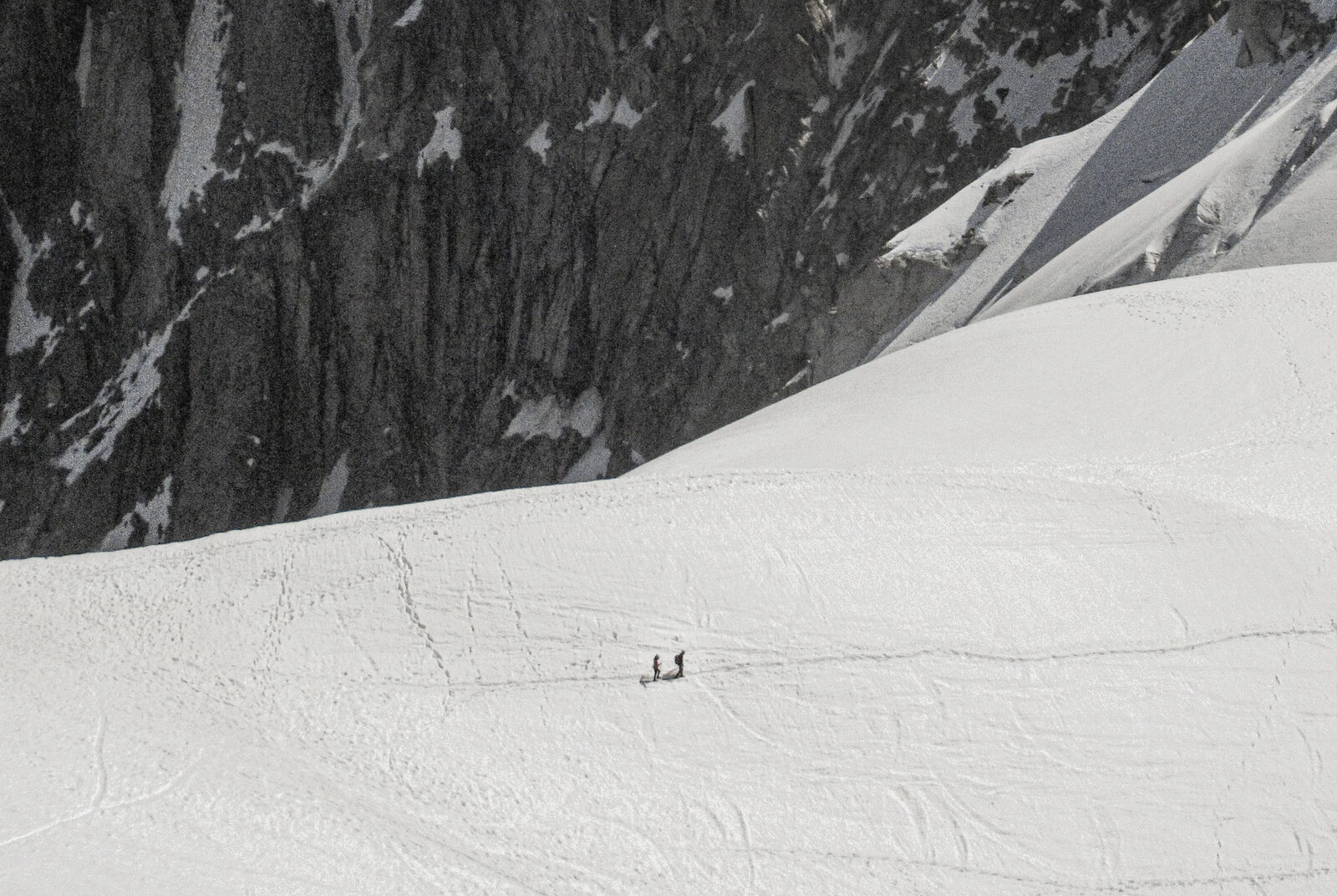 Two hikers dwarfed by a vast glacial face above Chamonix
