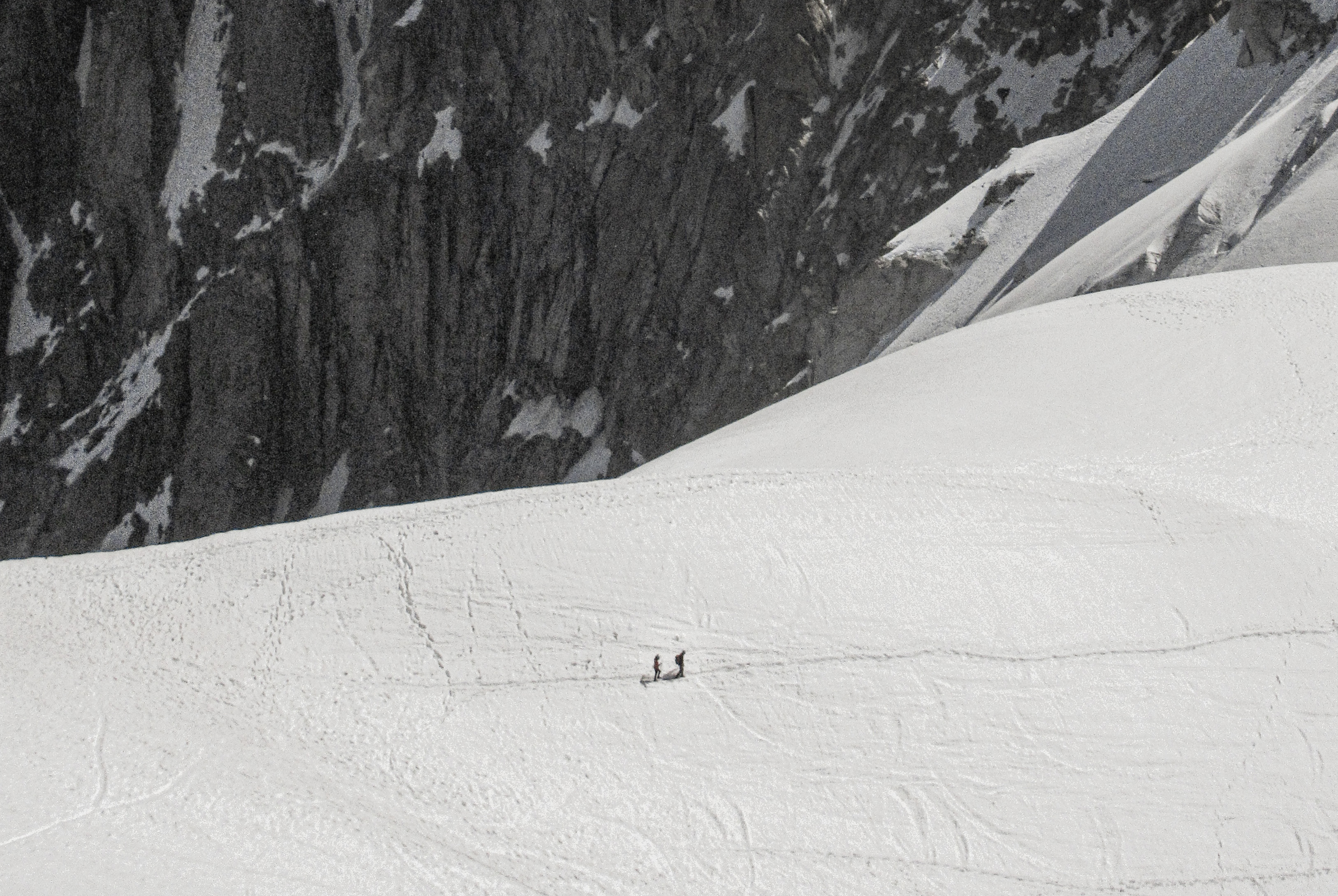 Two hikers dwarfed by a vast glacial face above Chamonix